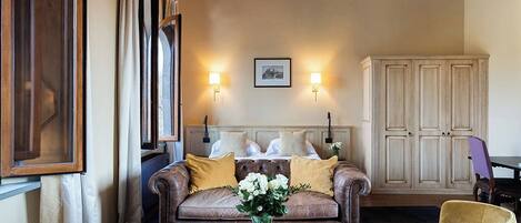 A cozy living room with a brown leather sofa, a glass coffee table with a vase of flowers, and a wooden cabinet.