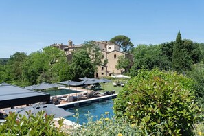 A pool area with lounge chairs and umbrellas, surrounded by greenery and a historic building in the background.