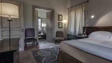 Habitación de hotel con cama, escritorio, silla, lámpara y baño visible a través de una puerta abierta.