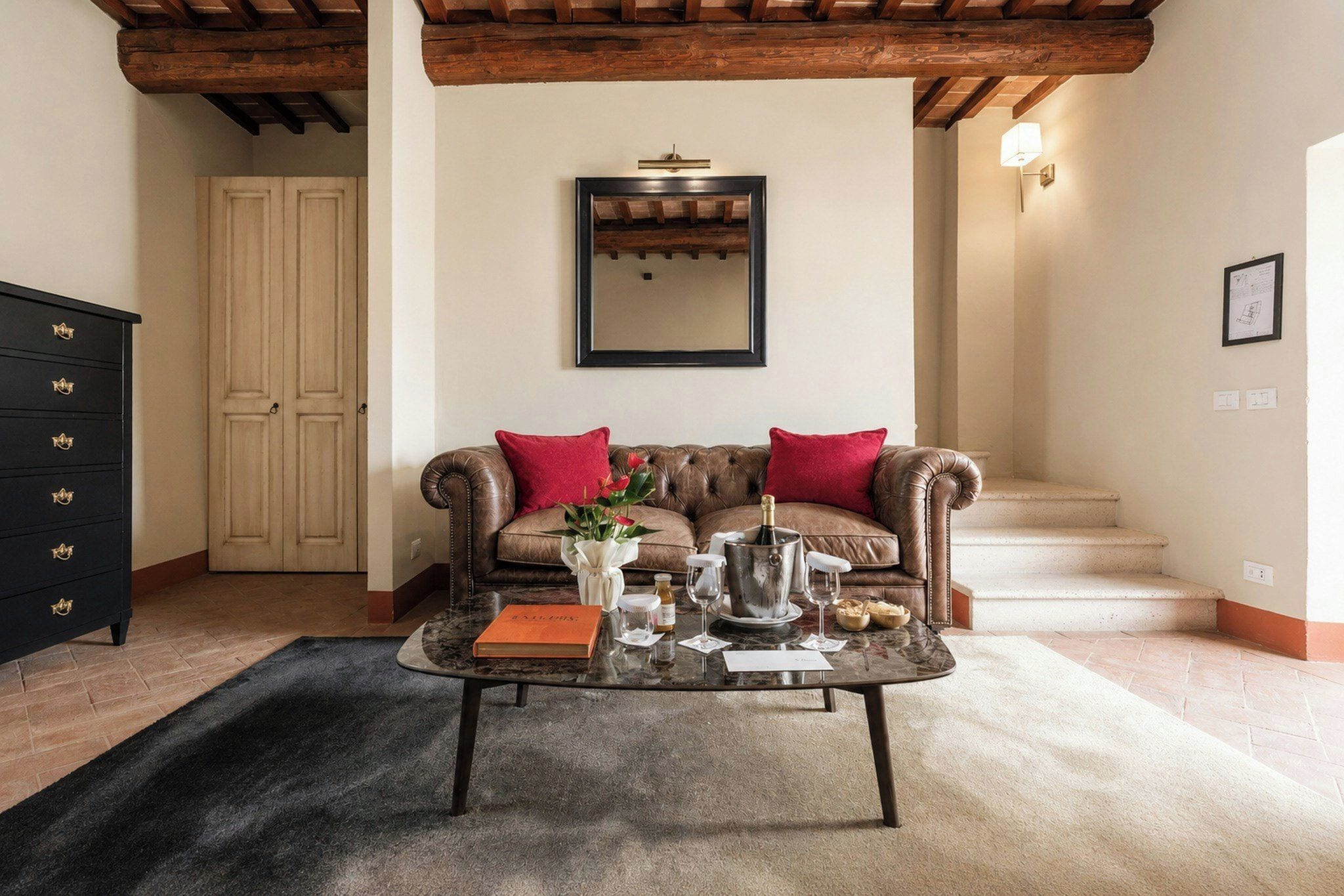 Una sala de estar con un sofá de cuero, una mesa de centro con varios objetos, un aparador de madera y una escalera.