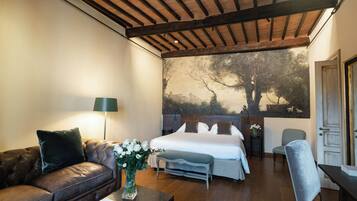 Una camera da letto con un letto grande, un'area salotto con divano e poltrona, un comodino con lampada e un muro decorato con un murale raffigurante un albero.
