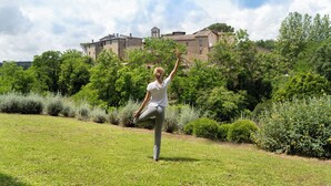 A person performing a yoga pose in a grassy area with a historic building in the background. - Castel Monastero - The Leading Hotels of the World (Castelnuovo Berardenga)