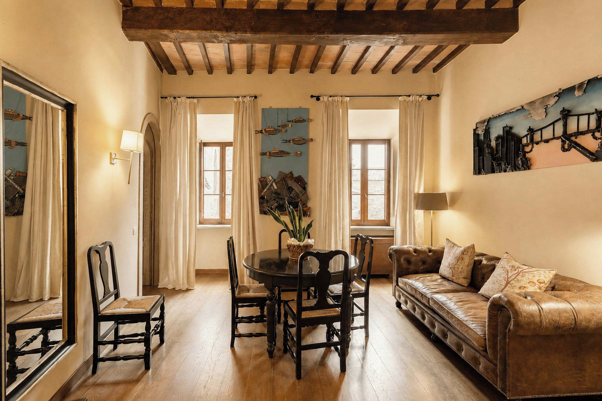 A room with a dining table, chairs, a sofa, and a painting on the wall.