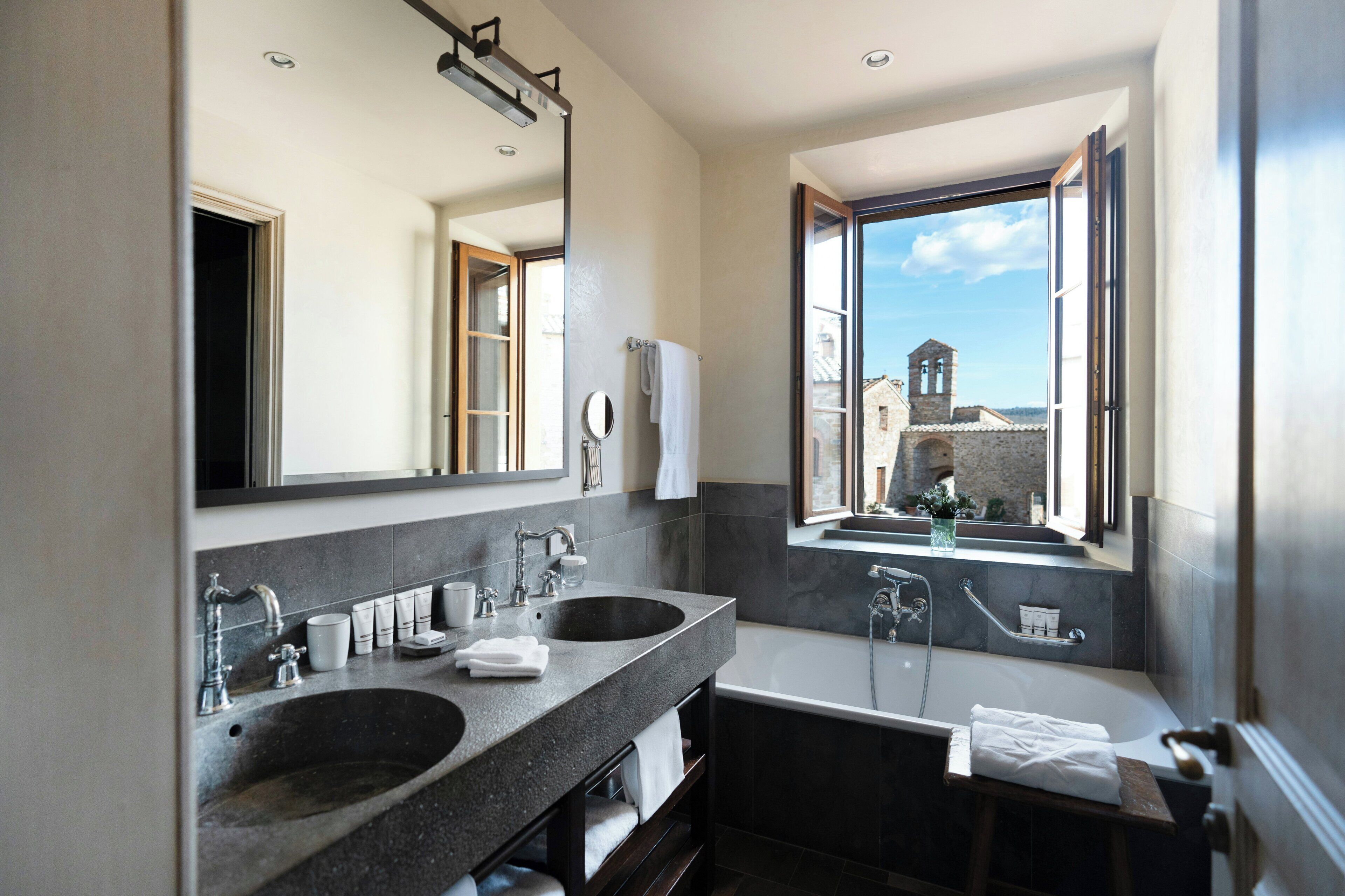A modern bathroom with two sinks, a large mirror, and a view of a historic building through a window.