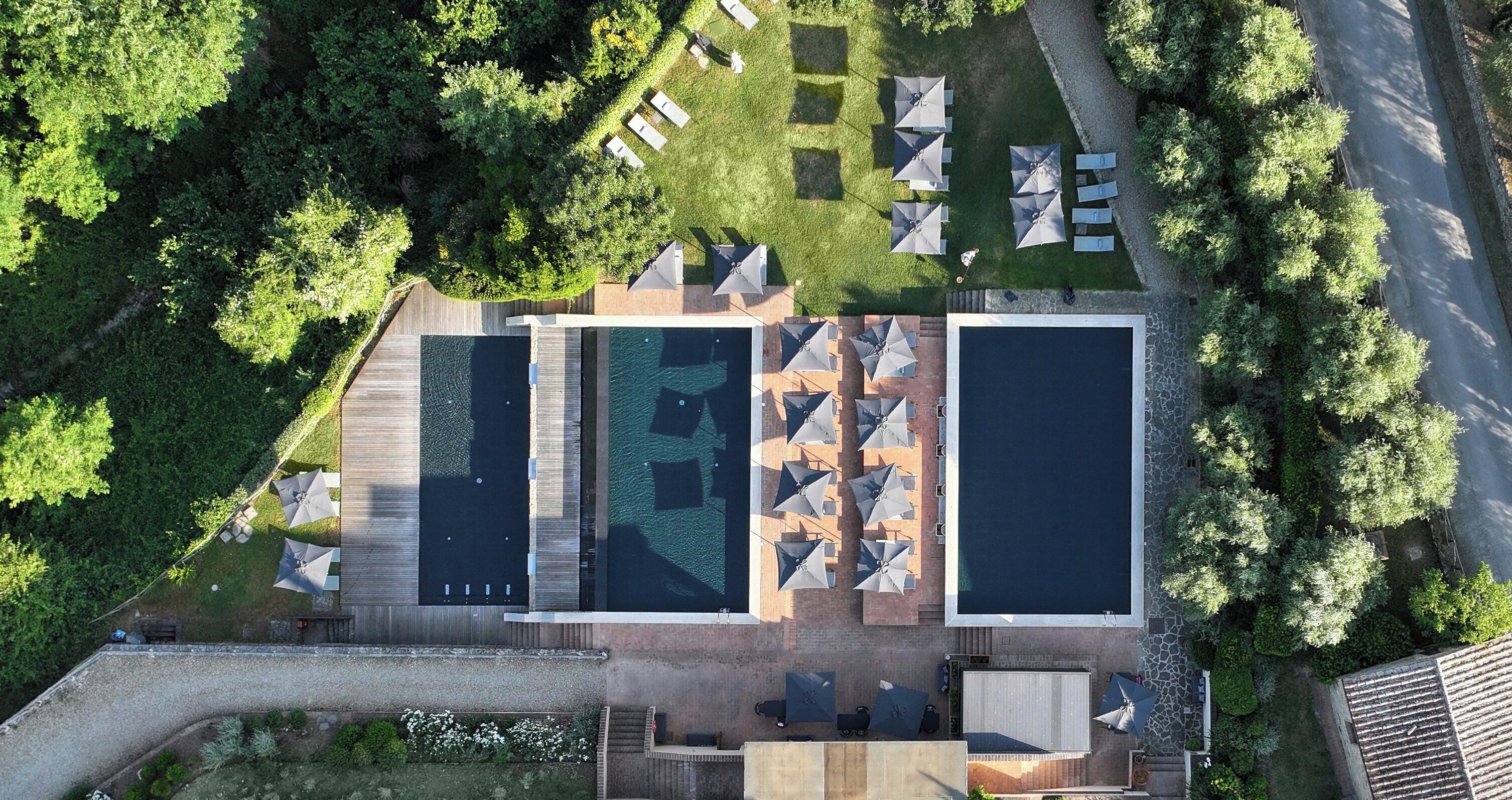 An aerial view of a resort with two swimming pools, outdoor seating, and lush greenery.
