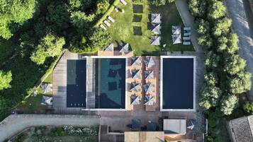 An aerial view of a resort with two swimming pools, outdoor seating, and lush greenery.