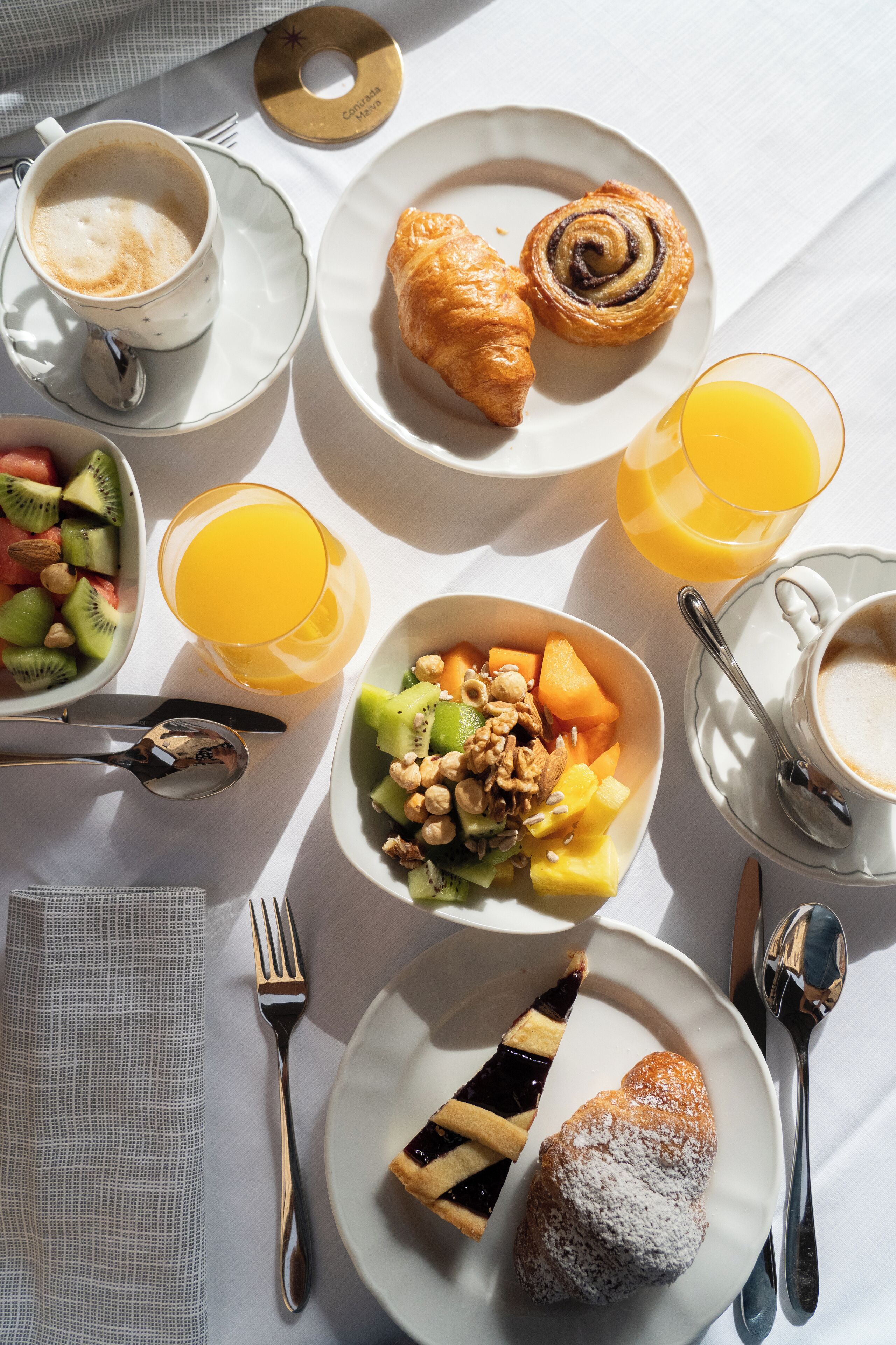 A breakfast setting with various dishes including croissants, fruit salad, and beverages.