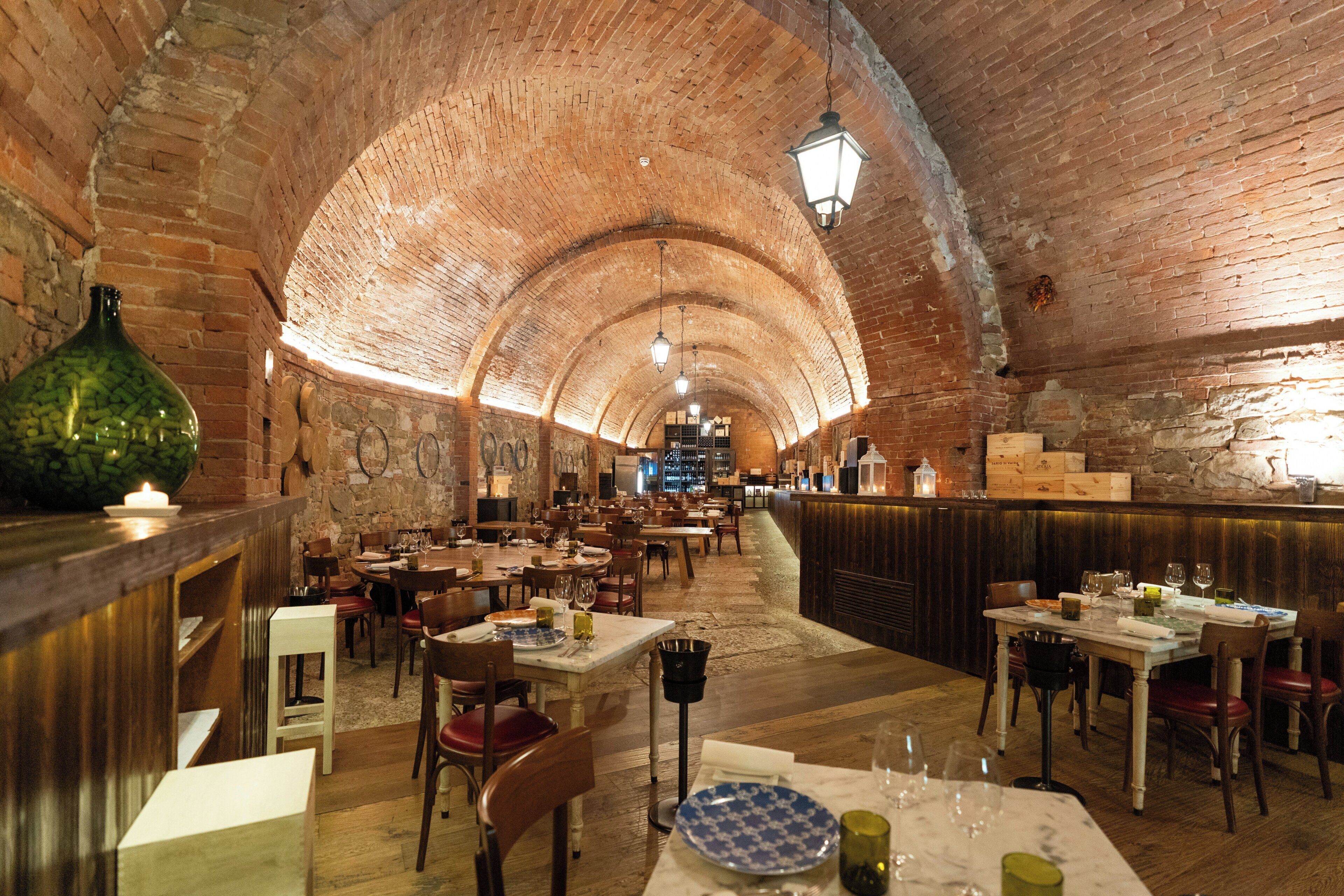 A restaurant with brick arches, wooden tables, and a bar area.