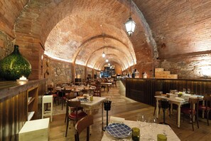 A restaurant with brick arches, wooden tables, and a bar area. - Castel Monastero - The Leading Hotels of the World (Castelnuovo Berardenga)