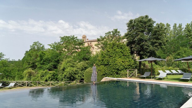 A swimming pool with lounge chairs and a person in a patterned dress. - Castel Monastero - The Leading Hotels of the World (Castelnuovo Berardenga)