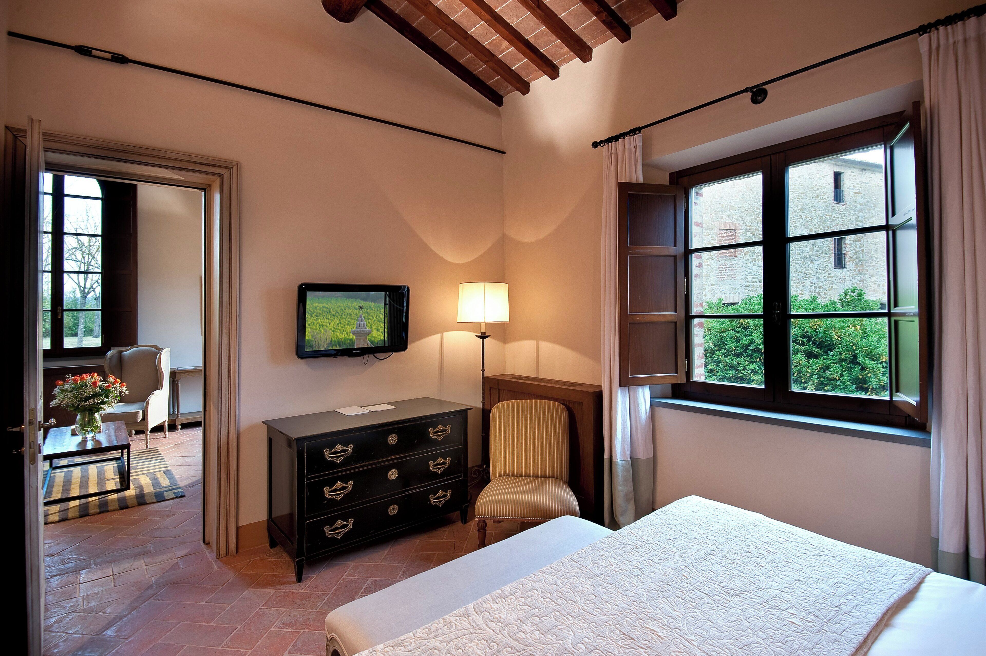 Quarto com cama, penteadeira, cadeira, TV e janela com vista para o verde.