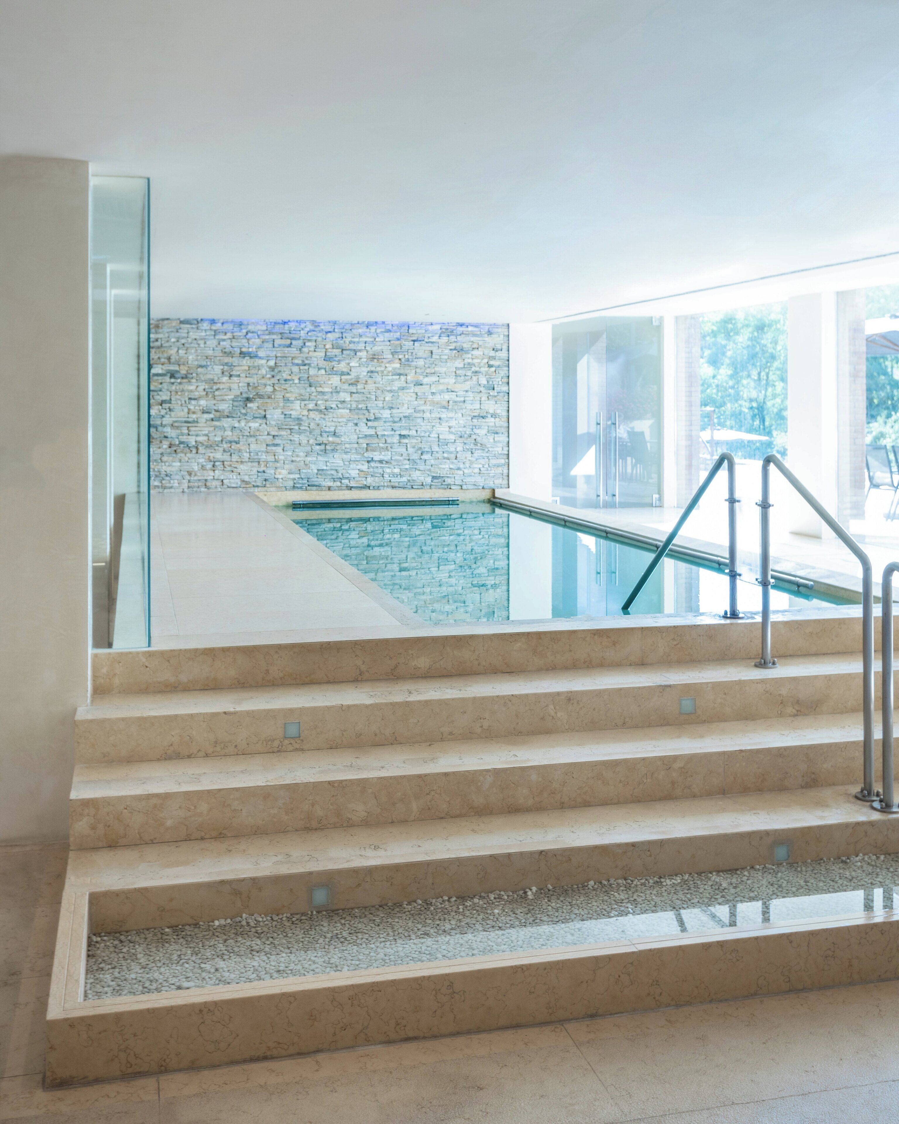 Un escalier moderne menant à un espace piscine agrémenté d’un mur en pierre et de rampes en verre.