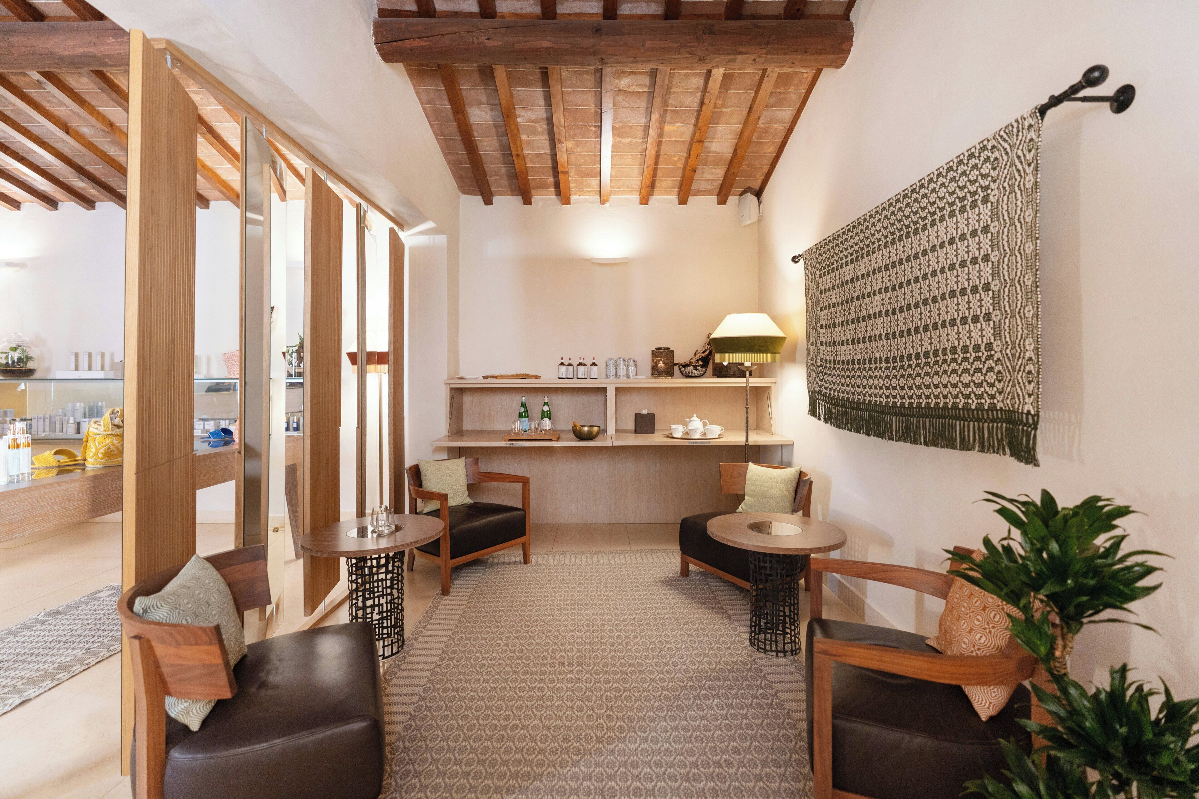A cozy room with a wooden ceiling, a patterned wall hanging, and a seating area with two chairs and a table.