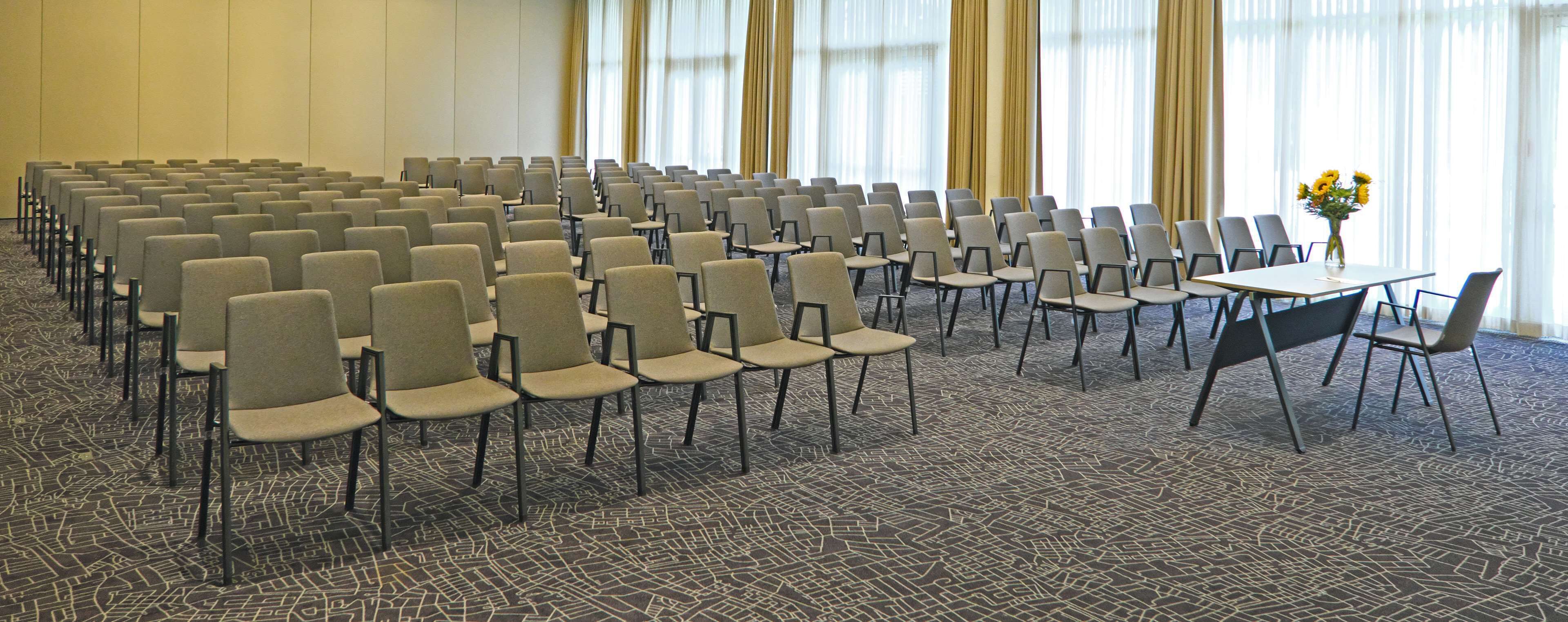 A conference room with rows of chairs, a table with chairs, and a vase with flowers.
