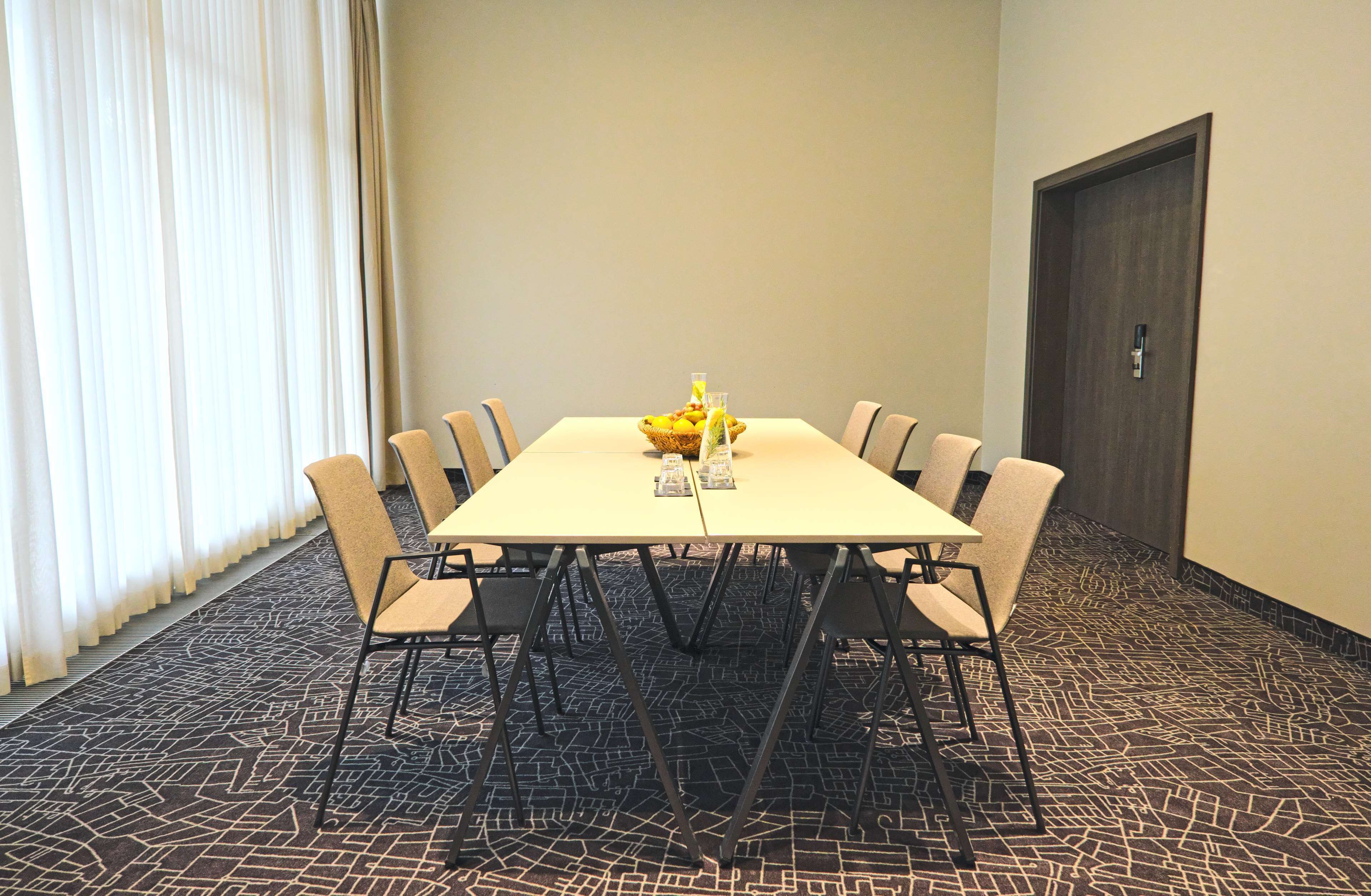 Un salón de conferencias con una mesa rectangular, ocho sillas, un frutero y una puerta.