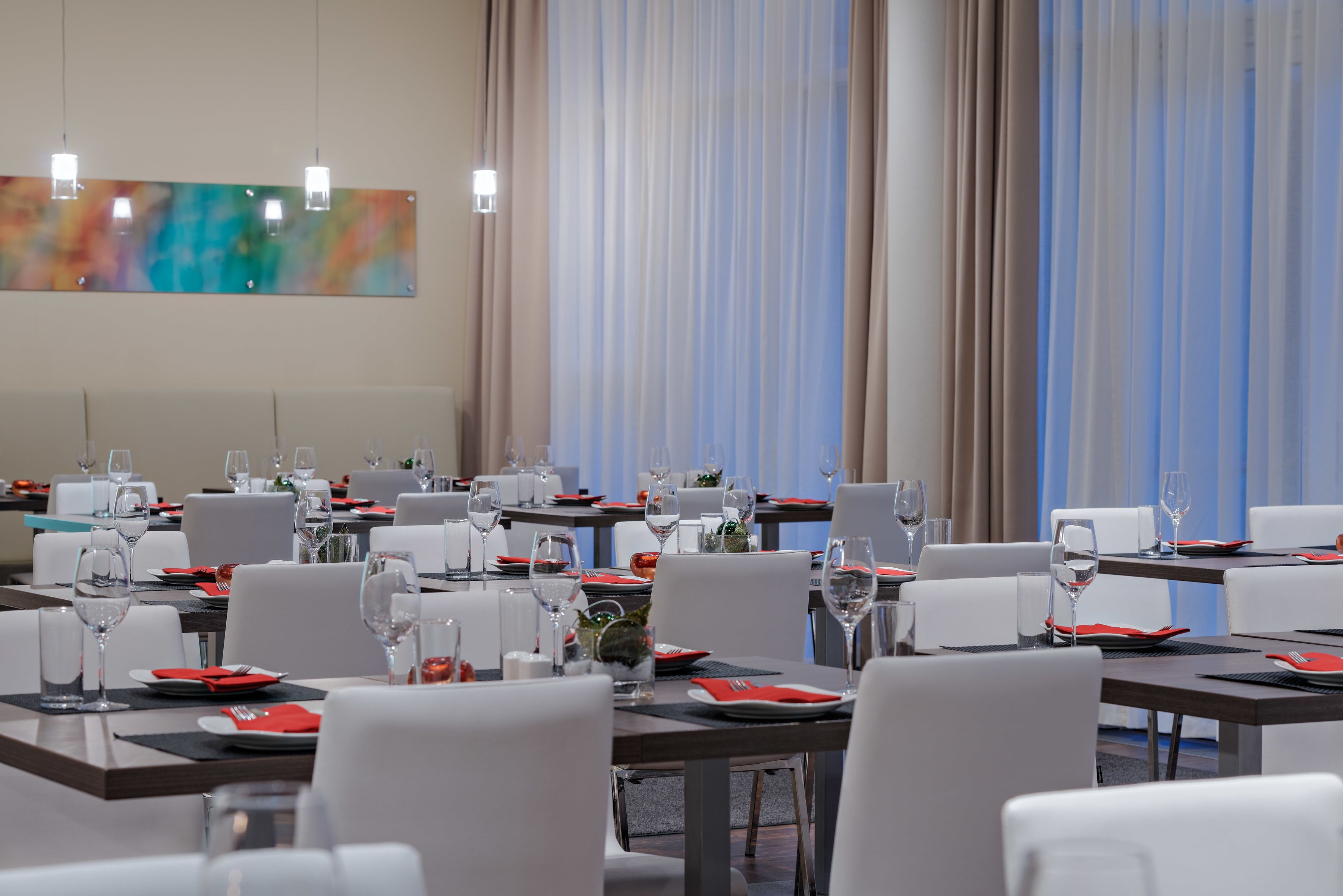 A dining area with tables set for meals, chairs, and a large abstract painting on the wall.
