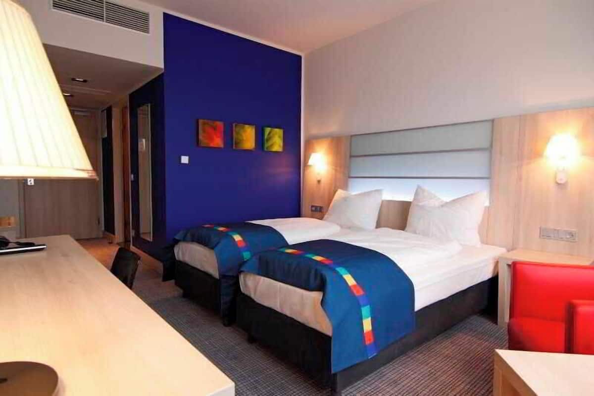 A hotel room with two beds, a desk, and a red chair.