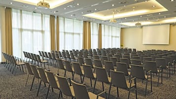 Un salón de conferencias con filas de sillas, una pantalla de proyector y piso alfombrado.