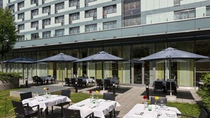 An outdoor dining area with tables and chairs, umbrellas, and a building in the background. - Park Inn by Radisson Linz (Linz)