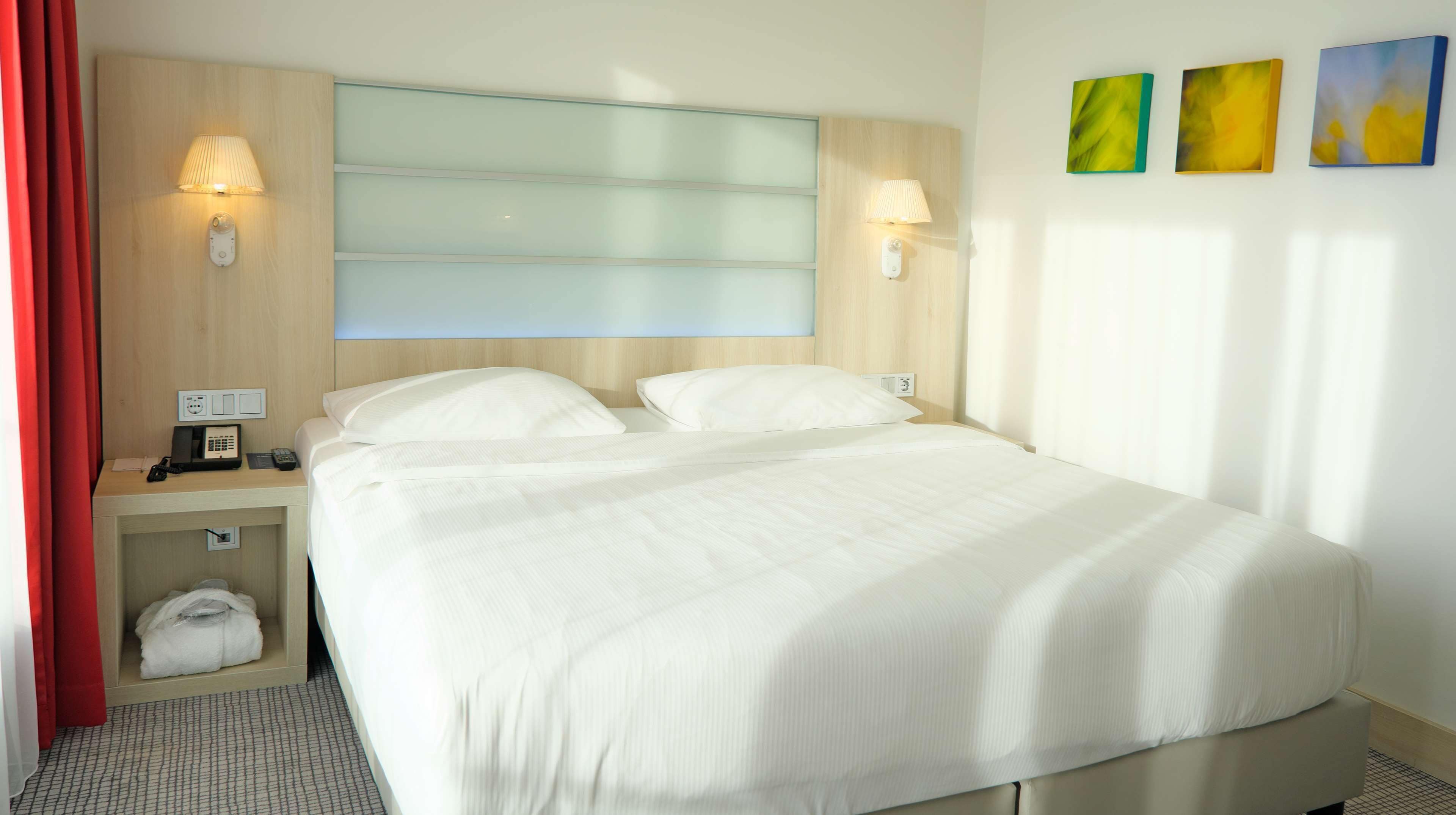 Habitación de hotel con una cama grande, dos mesitas de noche y dos lámparas de pared, además de una cortina roja.