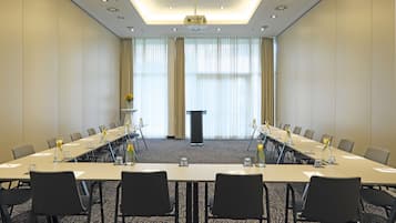 Un salón de conferencias con una larga mesa, sillas, un atril y un amplio ventanal con cortinas.