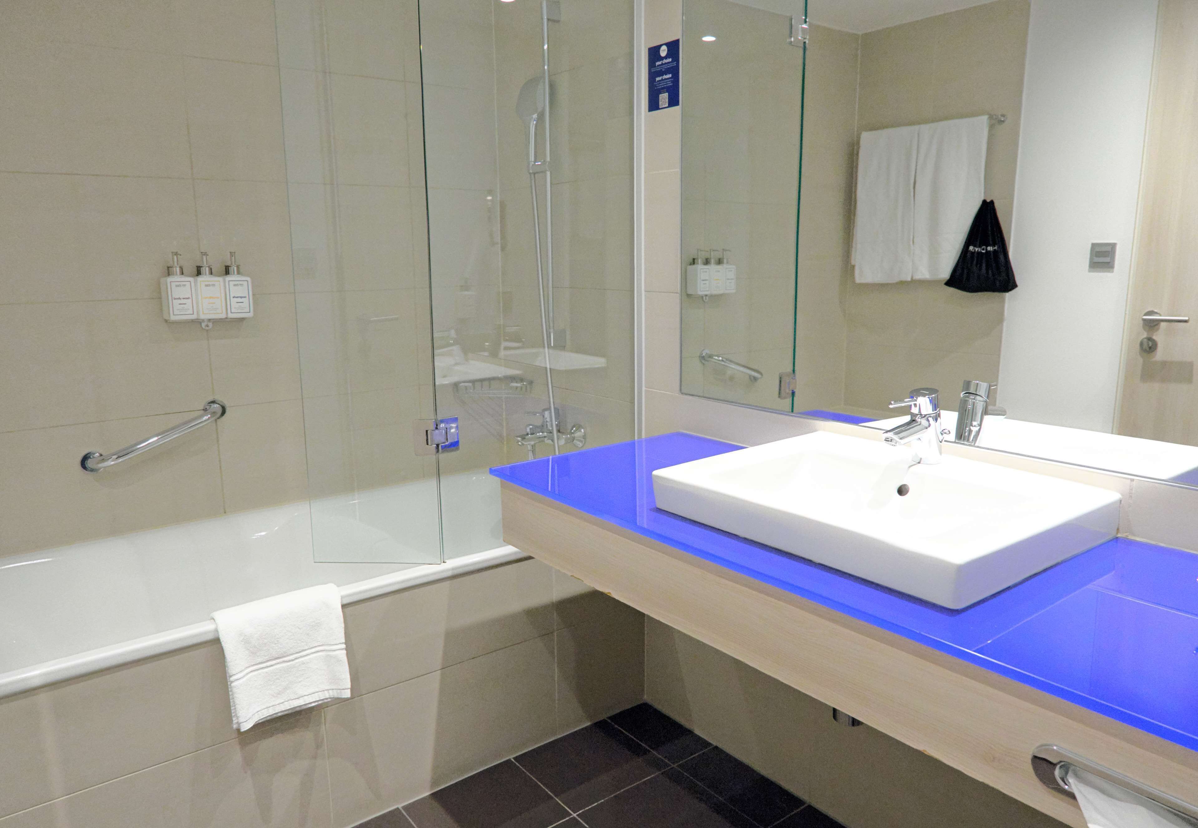 A modern bathroom with a glass-enclosed shower, a white sink with a blue countertop, and a large mirror.