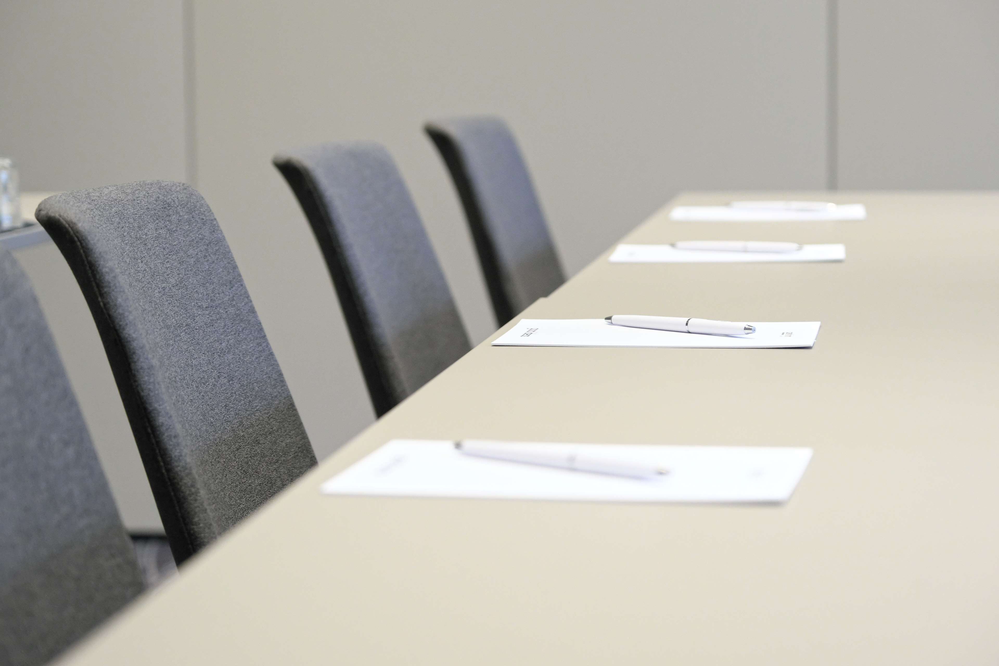 A conference room with a long table, several chairs, and documents with pens on them.