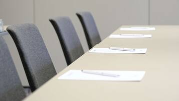A conference room with a long table, several chairs, and documents with pens on them.