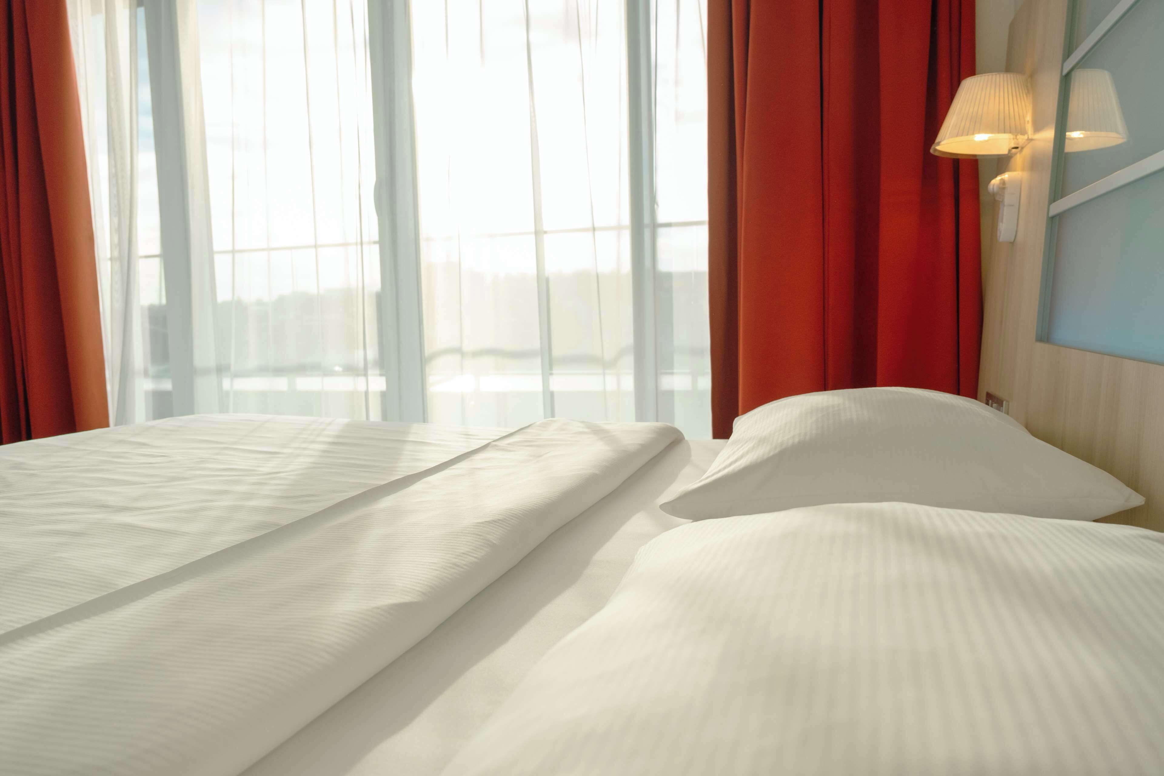 A hotel room with a large bed, red curtains, and a window with a view of buildings.