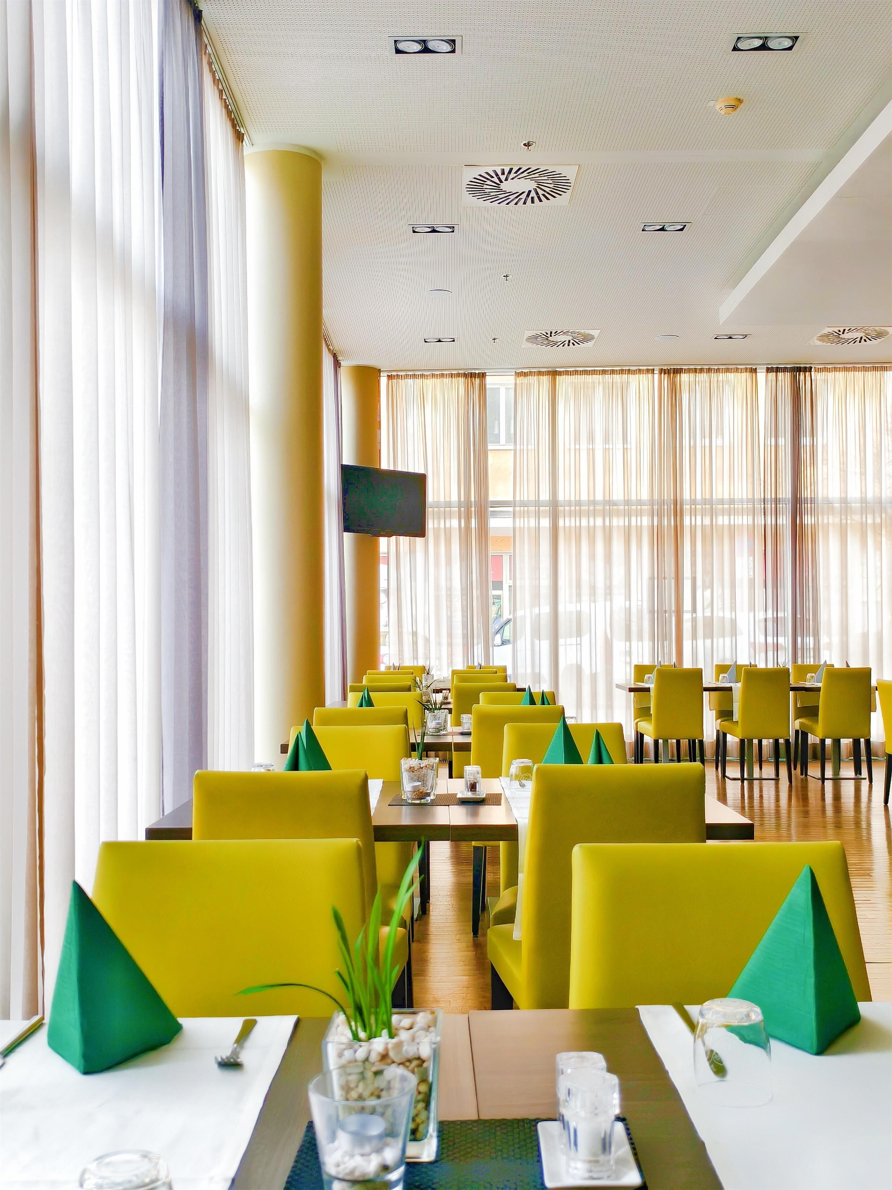 Ein Restaurant mit gelben Stühlen, Tischen und einem an der Wand befestigten Fernseher.