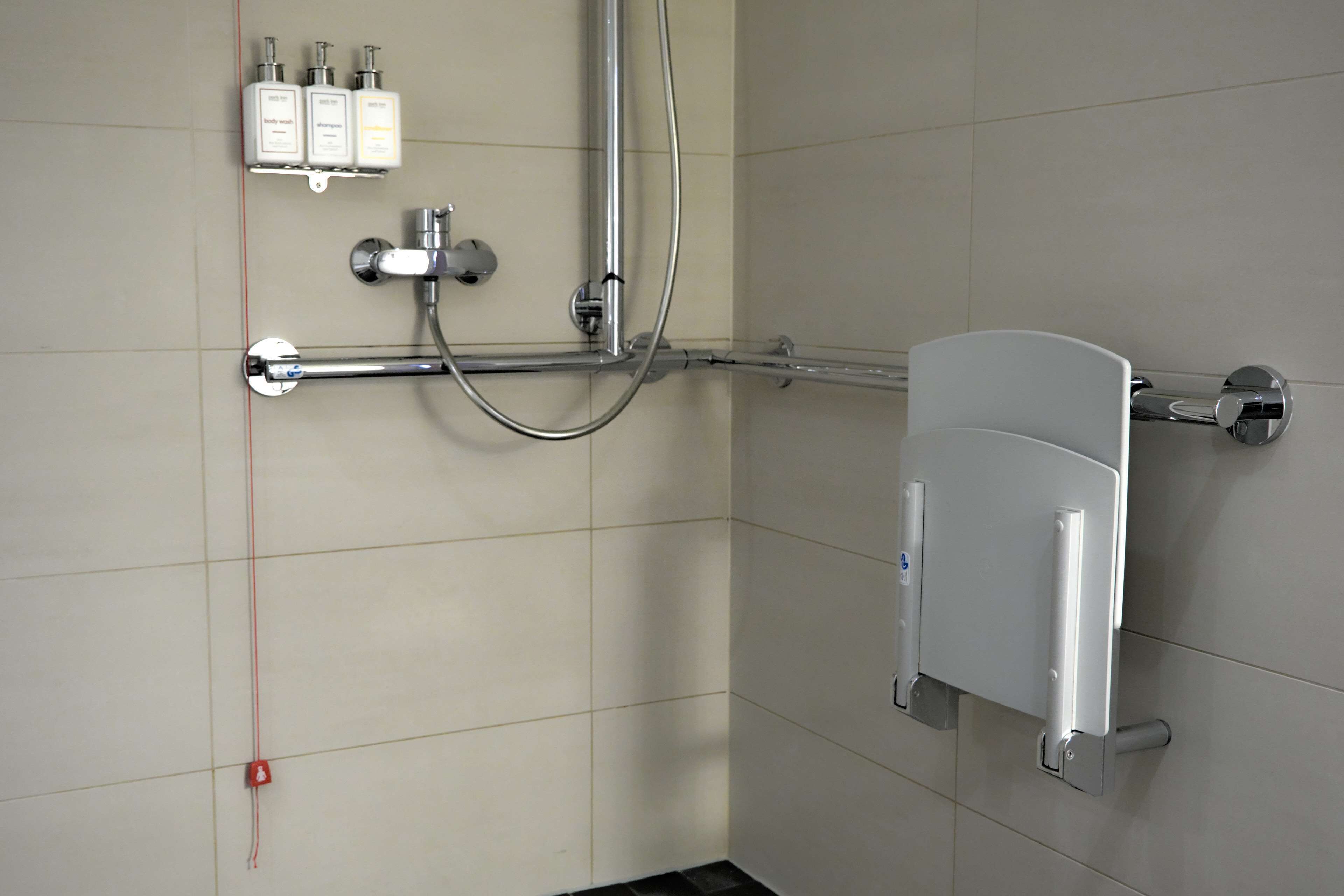 Un baño con ducha, un secamanos y tres botellas de jabón en un estante.