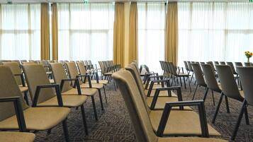 Un salón de conferencias con filas de sillas, ventanas amplias con cortinas y suelo alfombrado.
