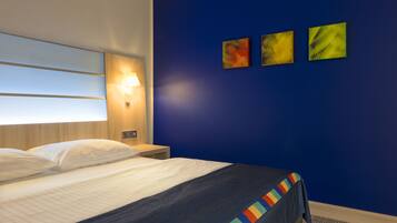 A hotel room with a bed, a nightstand, a wall-mounted lamp, and three abstract paintings.
