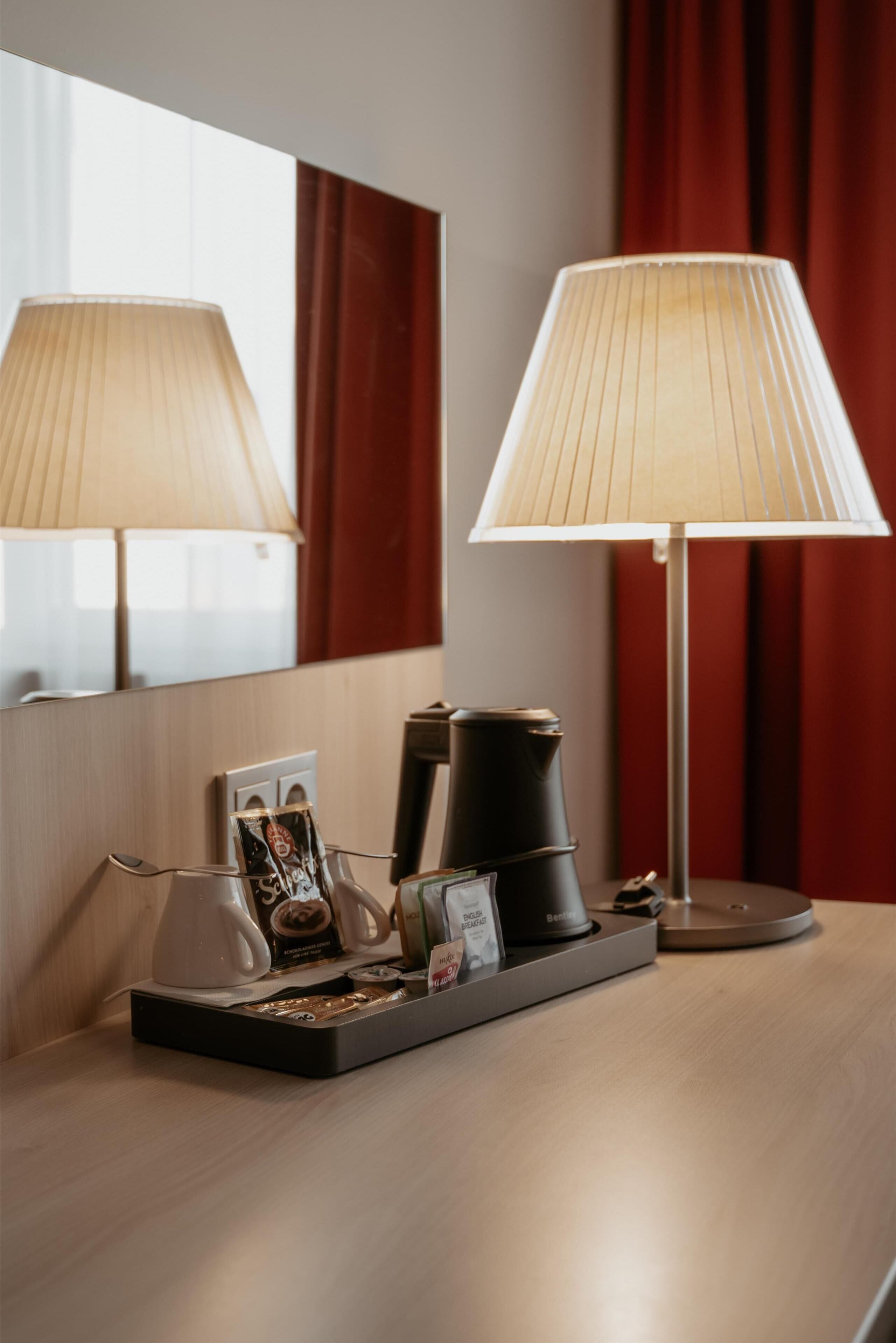 Et hotelværelse med et sengebord, der har en lampe, kaffemaskine og et bakke med en billedramme og en lille pyntegenstand.