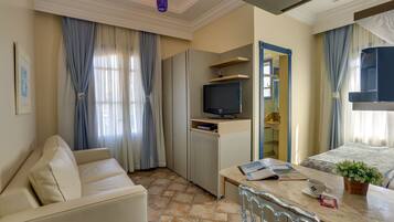 Habitación de hotel con sofá, mesa de comedor, televisor, cama y ventana con cortinas.