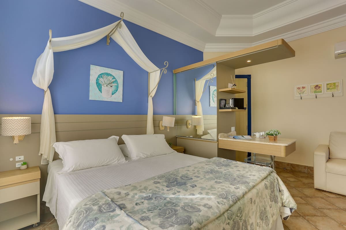 Un dormitorio con cama, mesitas de noche, un espejo, un escritorio y una silla.