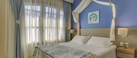 A bedroom with a bed, curtains, a nightstand, and a wall-mounted lamp.