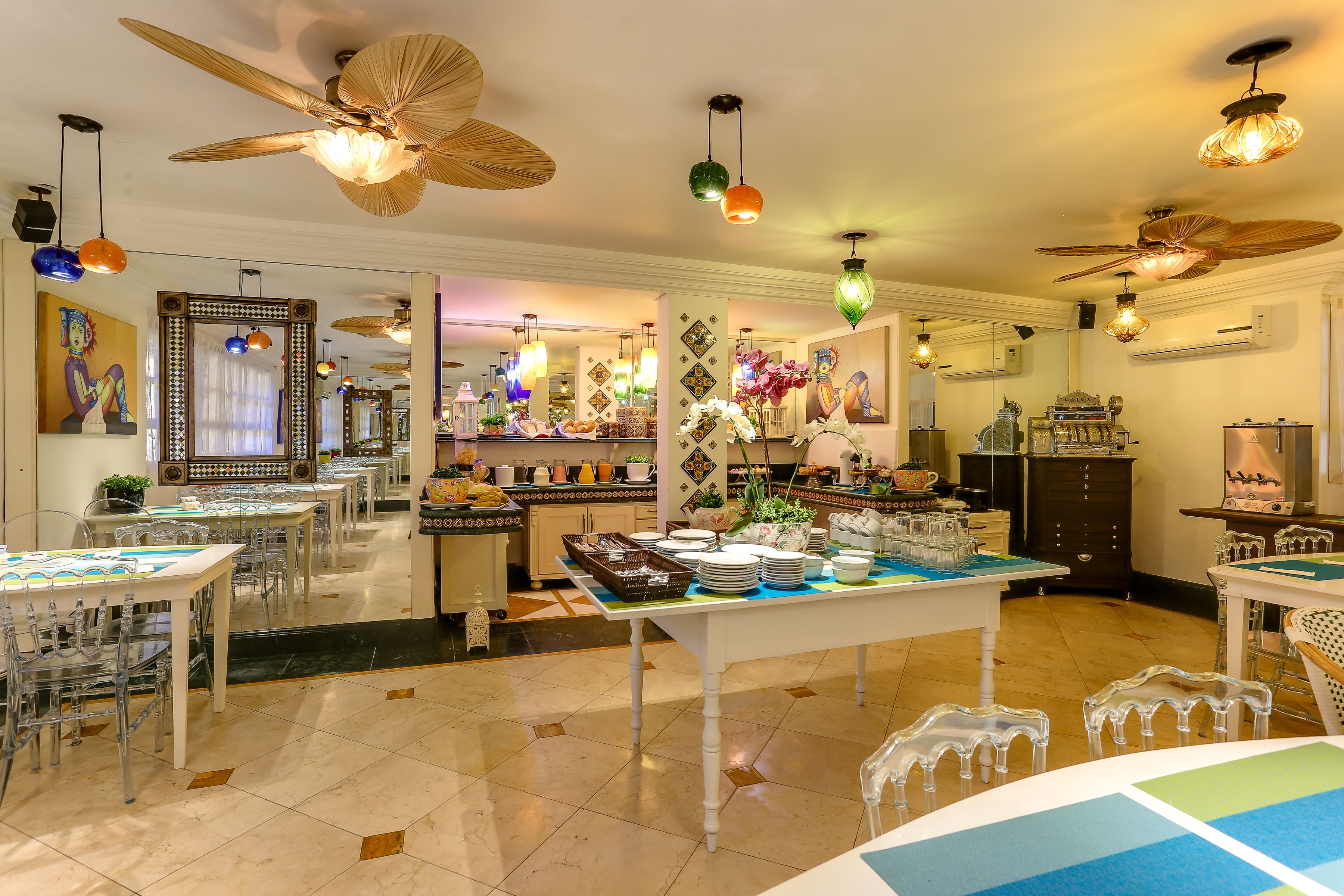 A spacious dining area with multiple tables and chairs, ceiling fans, and hanging lights.
