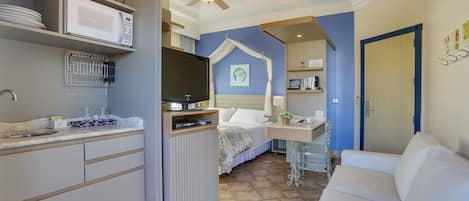 A compact hotel room with a kitchenette, a bed, a desk, and a seating area.
