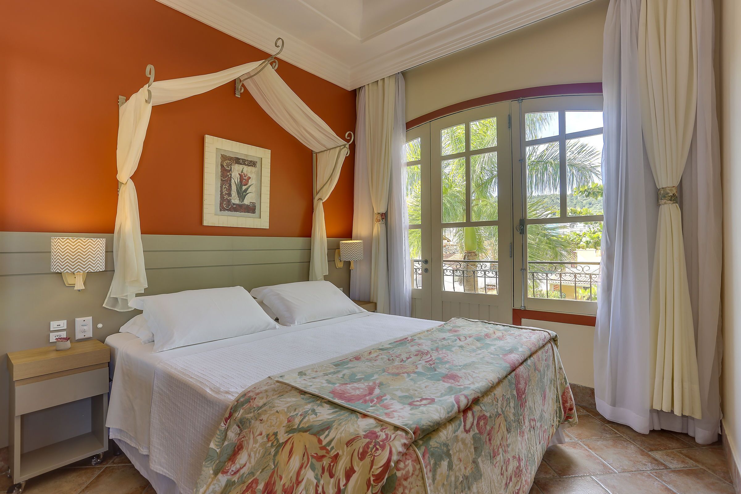 A bedroom with a canopy bed, a nightstand, a bedside table, and a window with curtains.