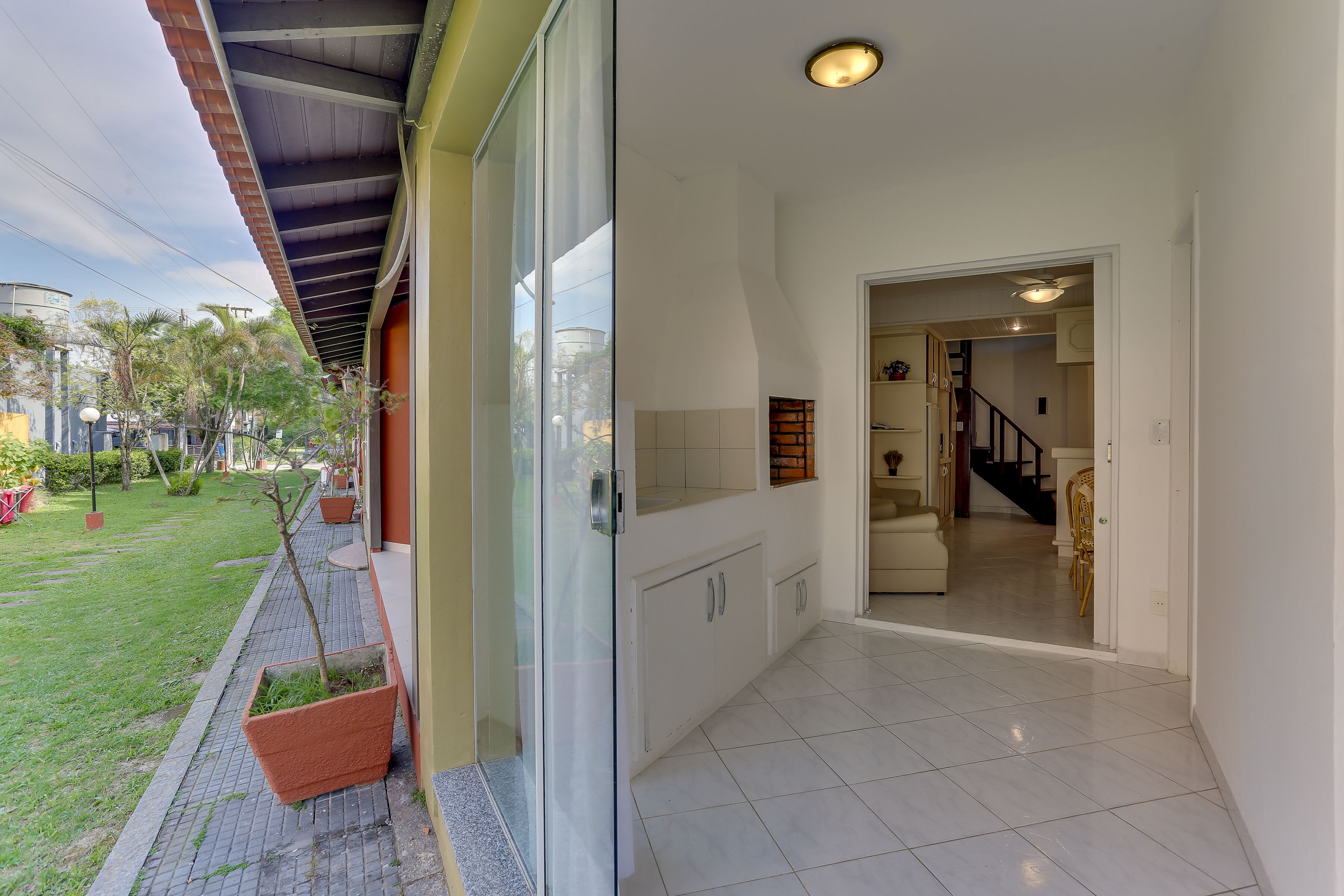 A modern interior with a glass door leading to a hallway, a tiled floor, and a view of a staircase.