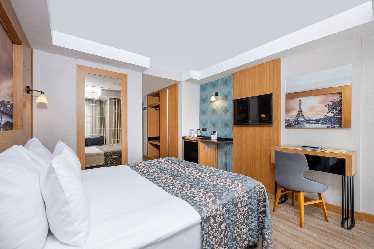 Ein Hotelzimmer mit einem Bett, einem Schreibtisch, einem Stuhl, einem Fernseher und einem Bildstempel des Eiffelturms.