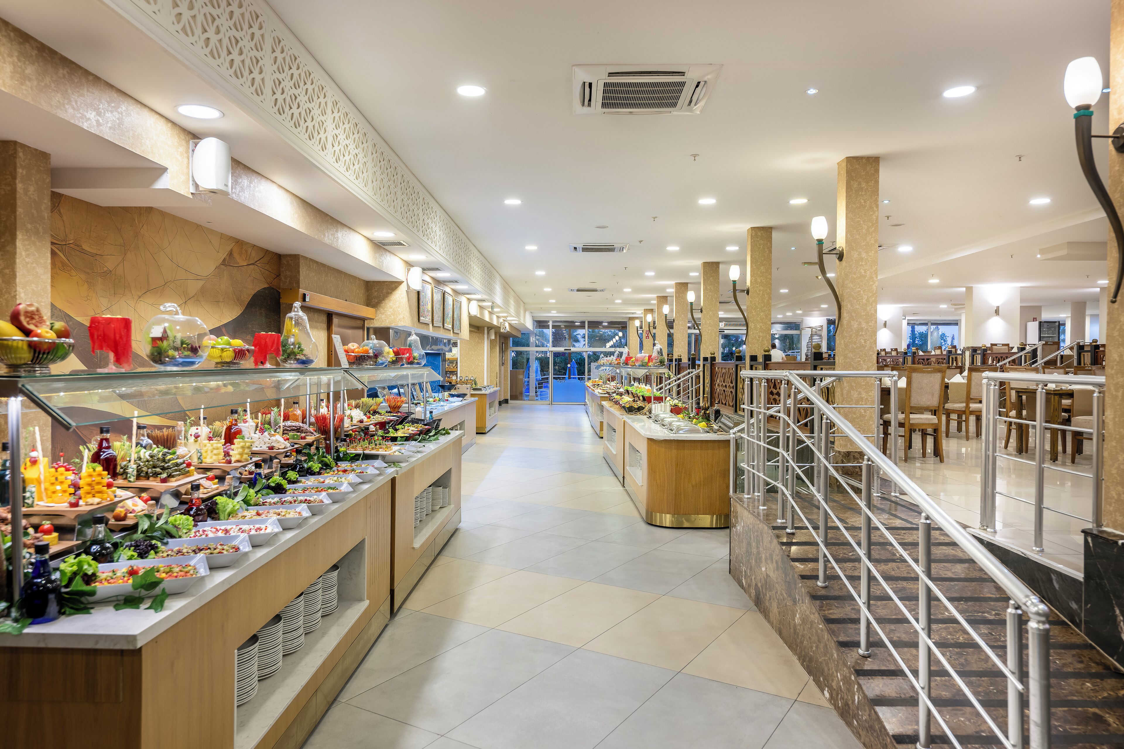 Un área de bufé con varias estaciones de comida, una escalera que conduce a un nivel superior y una decoración interior moderna.