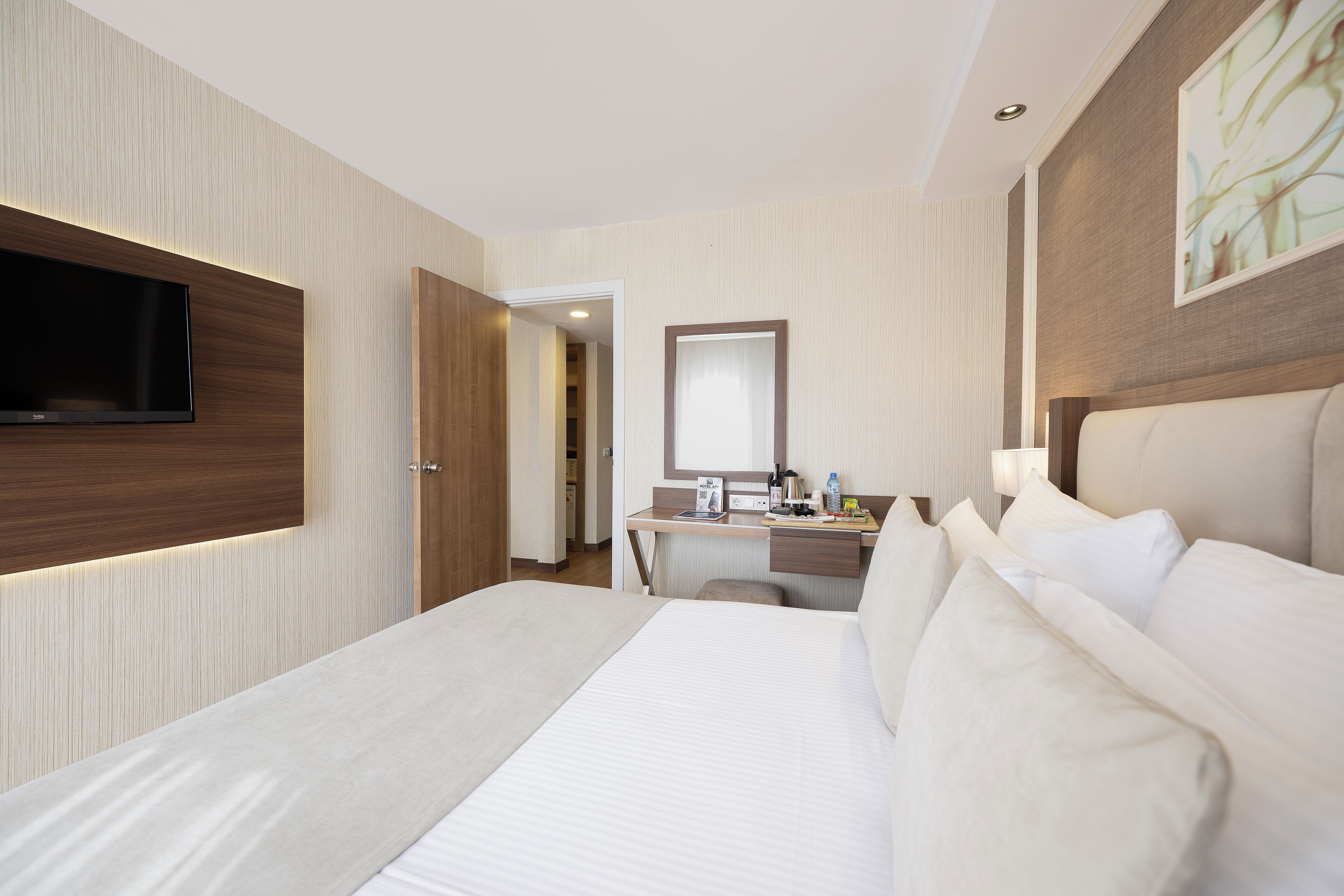 A hotel room with a large bed, a desk with a chair, a flat-screen TV mounted on the wall, and a mirror above the desk.