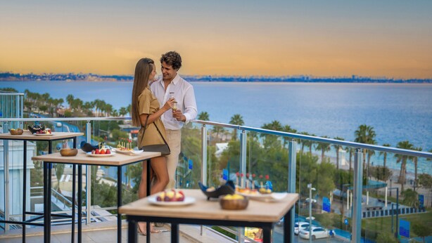 Una pareja cenando en un balcón con vistas al agua y al horizonte de una ciudad.