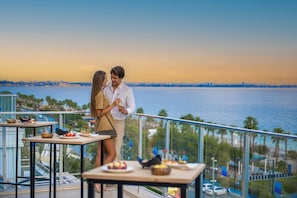 A couple dining on a balcony overlooking a body of water with a city skyline in the background. - Sealife Family Resort Hotel (Konyaalti)