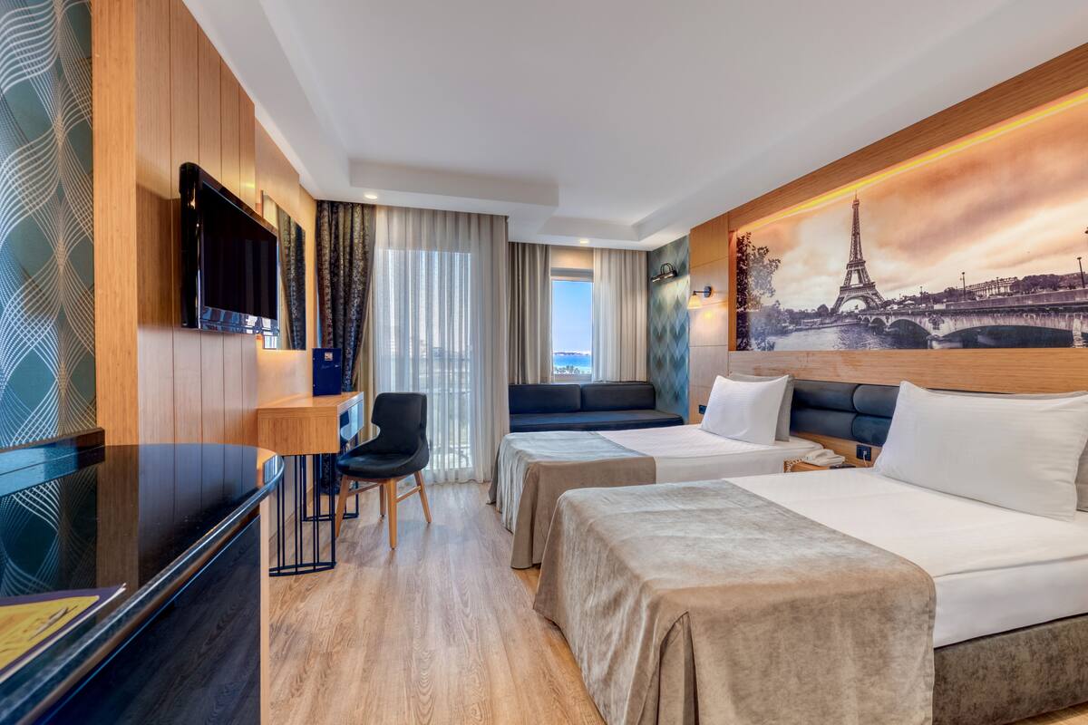 Ein Hotelzimmer mit zwei Betten, einem Schreibtisch, einem Fernseher und einem Bild des Eiffelturms.