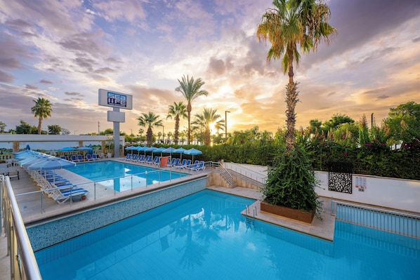 A swimming pool with lounge chairs and umbrellas, surrounded by palm trees and a sunset sky. - Sealife Family Resort Hotel (Konyaalti)