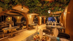 Un restaurante con una decoración moderna, que presenta mesas dispuestas para comer, un techo decorado con follaje e iluminación cálida.