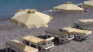 A beach with several yellow and white striped lounge chairs and beige umbrellas. - Paritsa Hotel (Kos)